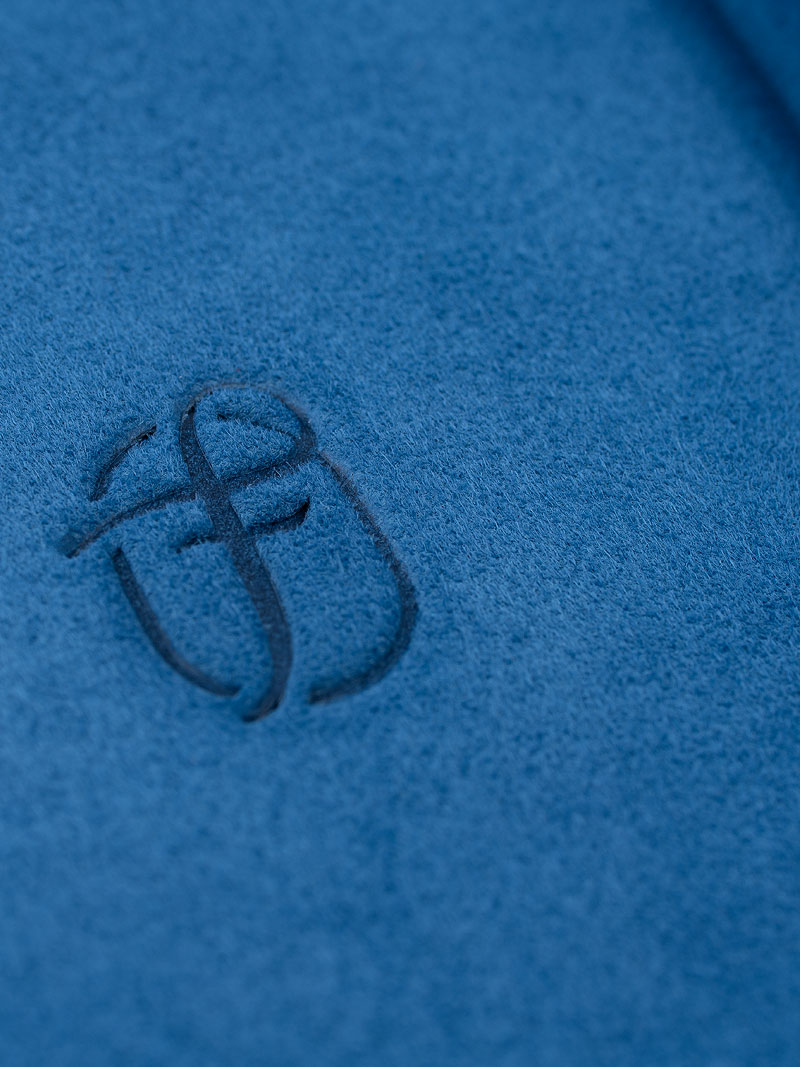 Detail einer Logo Blindprägung Fleur de Luxe auf blauem echtem Veloursleder