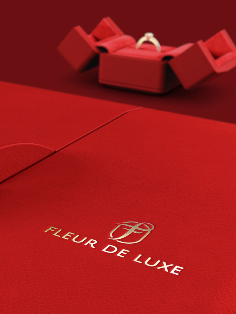 Detail eines Fleur de Luxe Collieretuis rot mit Logo Goldfolien-Prägung, im Hintergrund Ringetui rot geöffnet