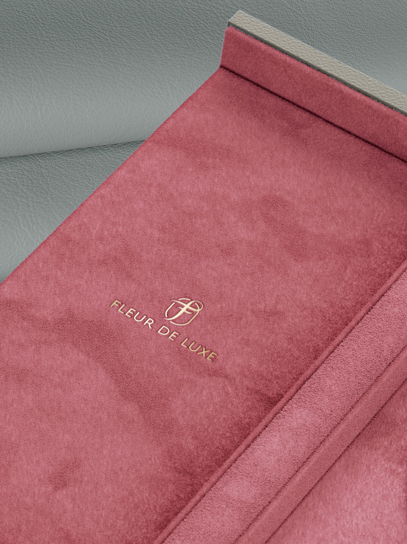 Detail eines Fleur de Luxe Collieretuis mit Logo Goldfolien-Prägung in Rosé-fluo, liegend auf Kalbsleder in Grey-Brown