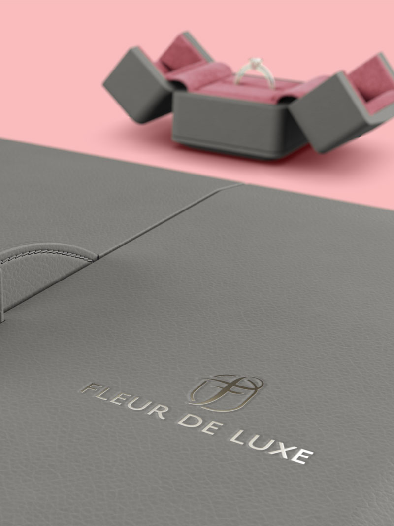 Detail Fleur de Luxe Collieretuis in Grey-Brown mit Logo Silberfolienprägung, im Hintergrund ein geöffnetes Ringetui